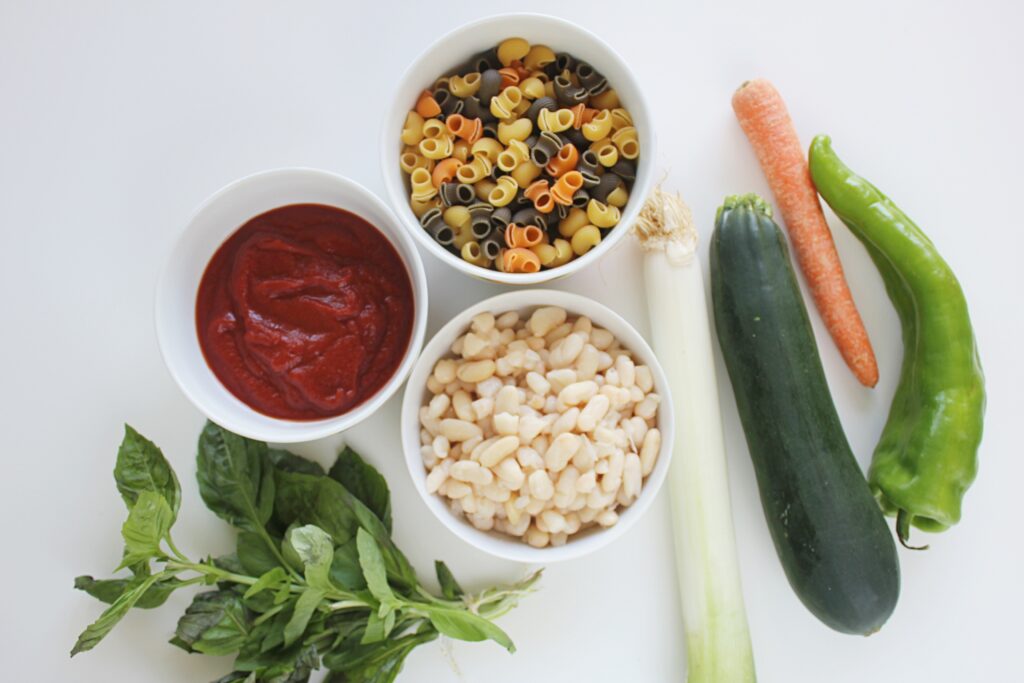 ingredients for minestrone soup: white beans, bell pepper, carrot, zucchini, leek, pasta, fresh herbs